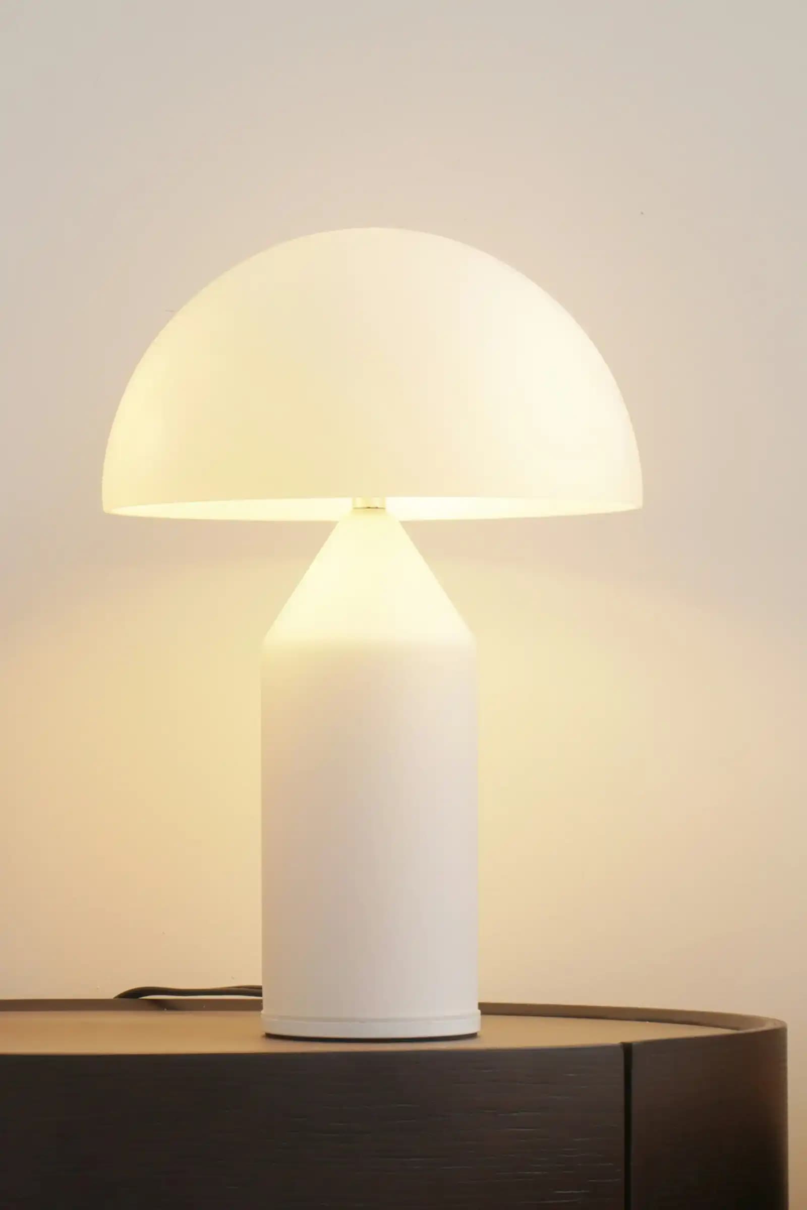 Tänd vit bordslampa på ett mörkt sidobord mot en ljus vägg